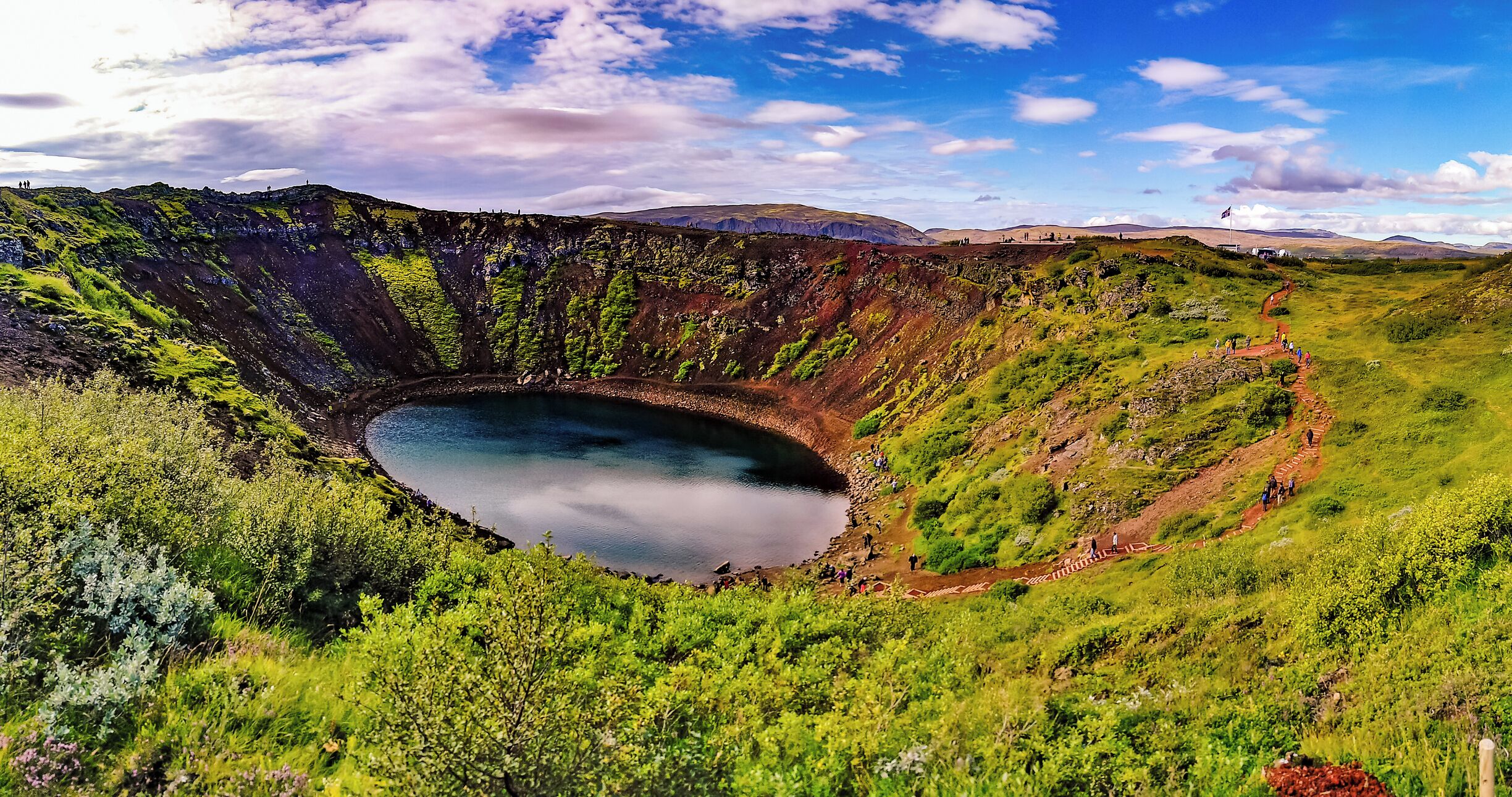 A large crater lake surrounded by green hills and mountains.