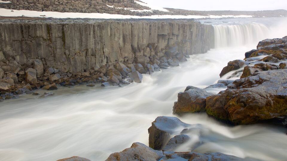 A waterfall cascading over a rocky cliff with snow patches on the ground.