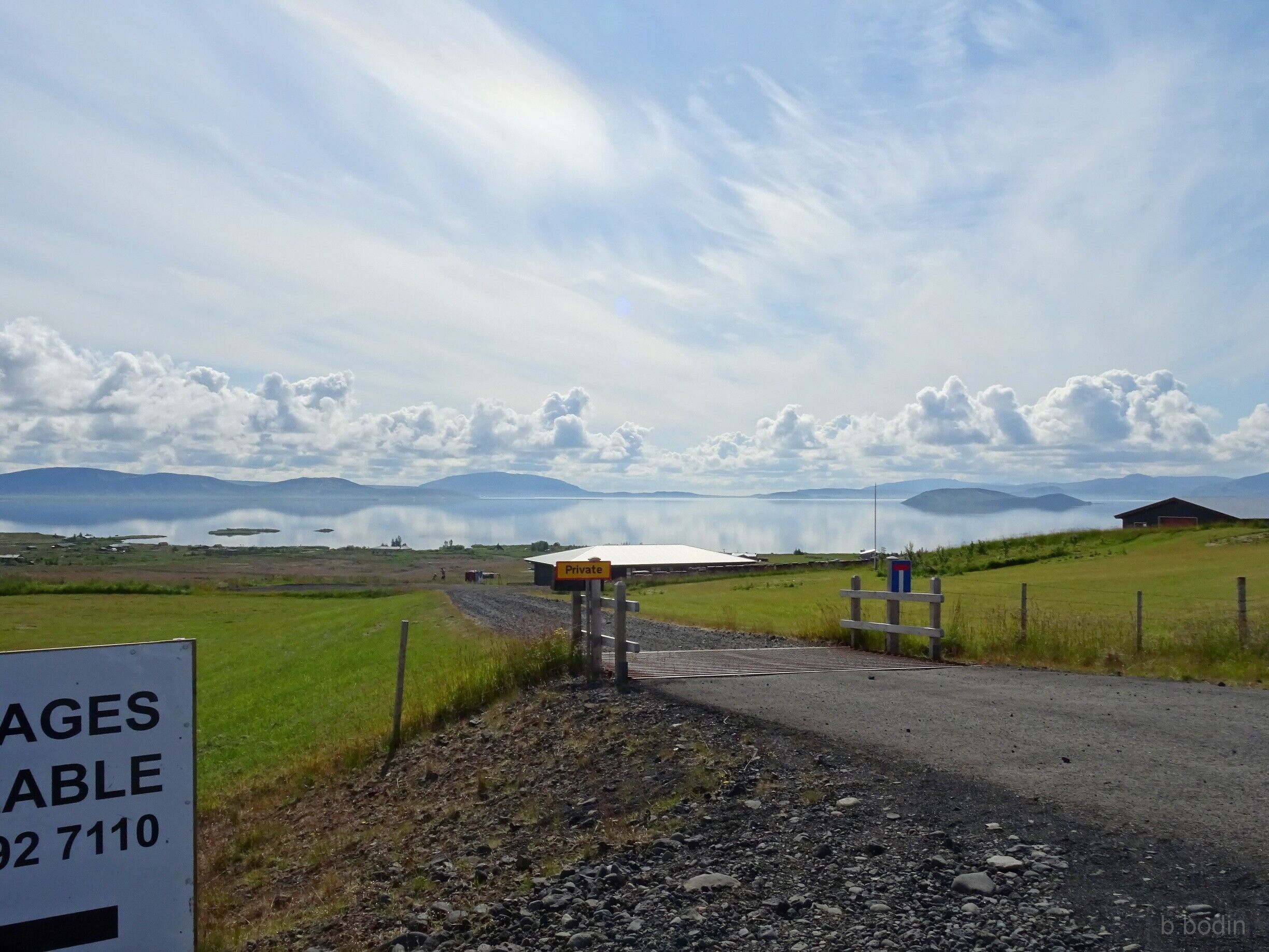 A rural landscape with a private property sign, a gravel road, and a body of water in the background.