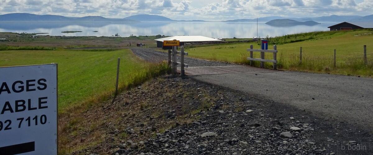 A rural landscape with a private property sign, a gravel road, and a body of water in the background.