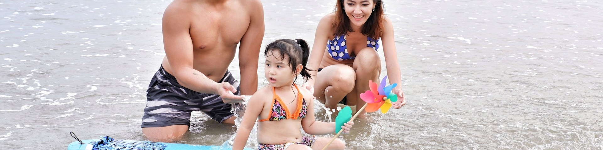 A beach scene with a child on a surfboard, an adult, and a woman.