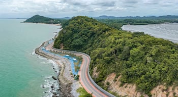 A coastal road winding along a cliffside, overlooking a calm sea and a forested mountain.