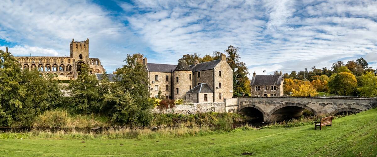 A historic stone building with a tower, a bridge, and lush greenery.