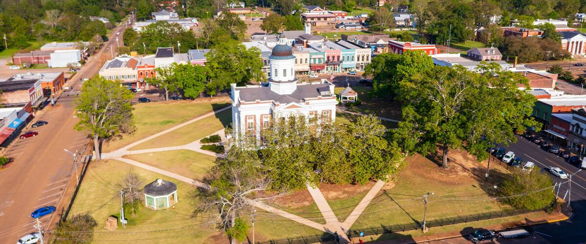 An aerial view of a town with historic buildings, a large white church with a dome, and a central square.