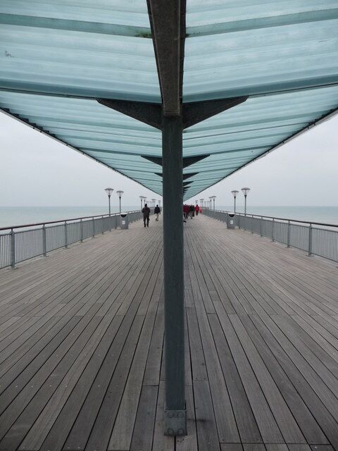 A wooden boardwalk with a glass canopy, leading to the sea.