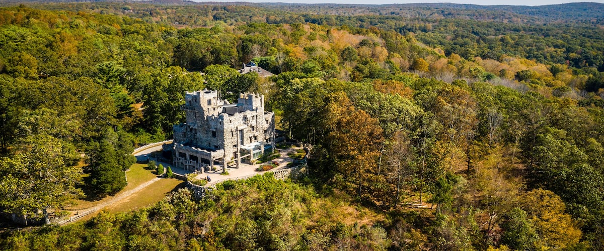A historic stone castle surrounded by dense forest and rolling hills.