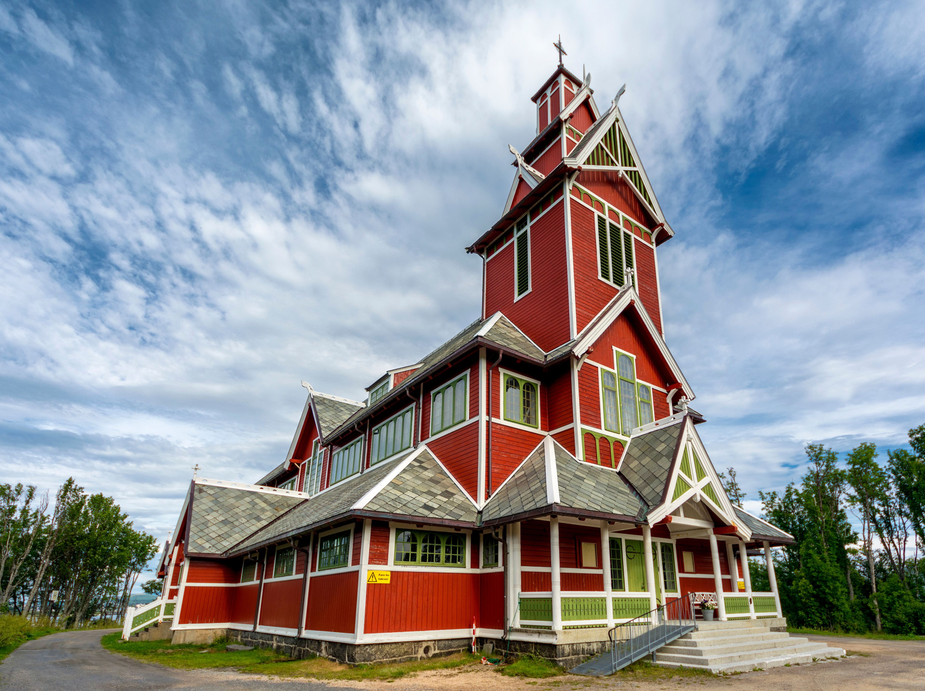 Una iglesia de madera roja con un tejado empinado y un campanario.