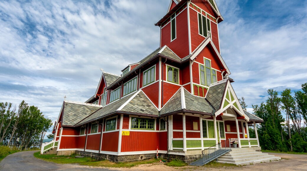 Una iglesia de madera roja con un tejado empinado y un campanario.
