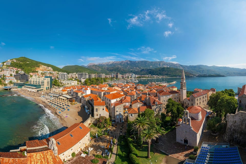 A coastal town with a historic fort, a beach, and a mountain backdrop.