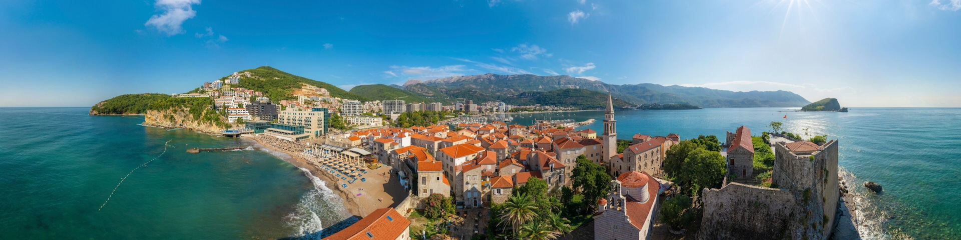Une ville cĂŽtiĂšre dotĂ©e dâun fort historique, dâune plage et bordĂ©e par une chaĂźne de montagnes.