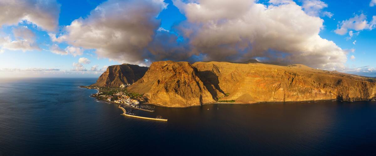 A coastal landscape with a prominent rocky island, a pier, and a small settlement.