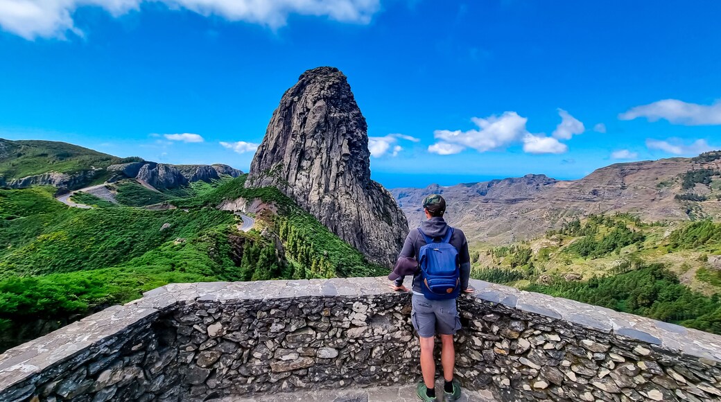 Sport man with backpack standing in front of massive volcanic rock formation Roque de Agando in Garajonay National Park on La Gomera, Canary Islands, Spain, Europe. Hiking trail on sunny day in summer