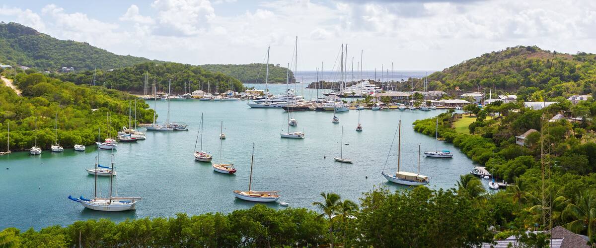 A marina with numerous sailboats docked, surrounded by lush greenery and hills.
