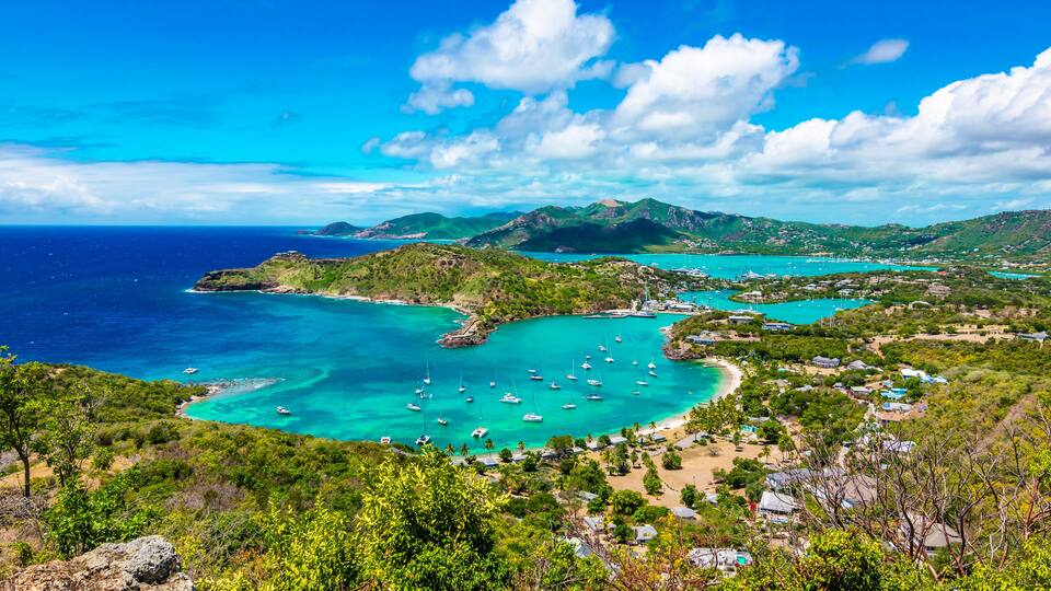 A coastal landscape with turquoise waters, boats, and a mountainous backdrop.