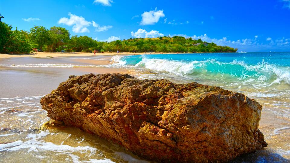 A rocky outcrop on a beach with clear turquoise water and a distant tree-covered island.
