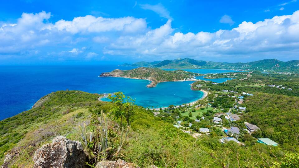 A coastal landscape with a bay, green hills, and scattered buildings.