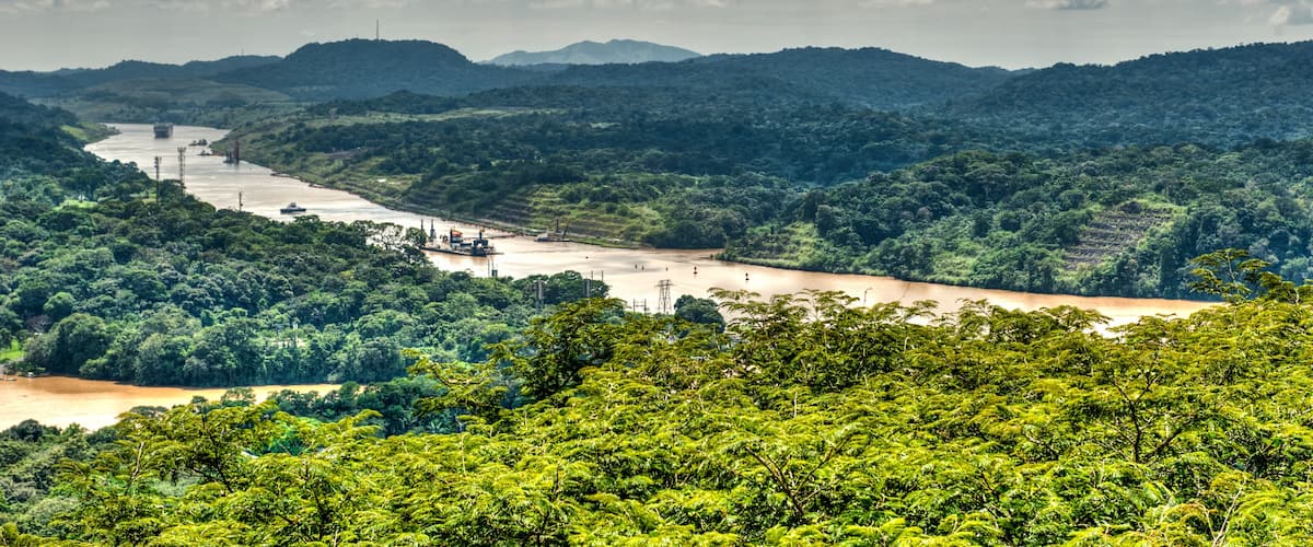 A river winding through a lush green valley with hills in the background and a cloudy sky above.