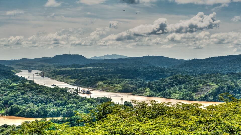 A river winding through a lush, green landscape with hills in the background and a cloudy sky.