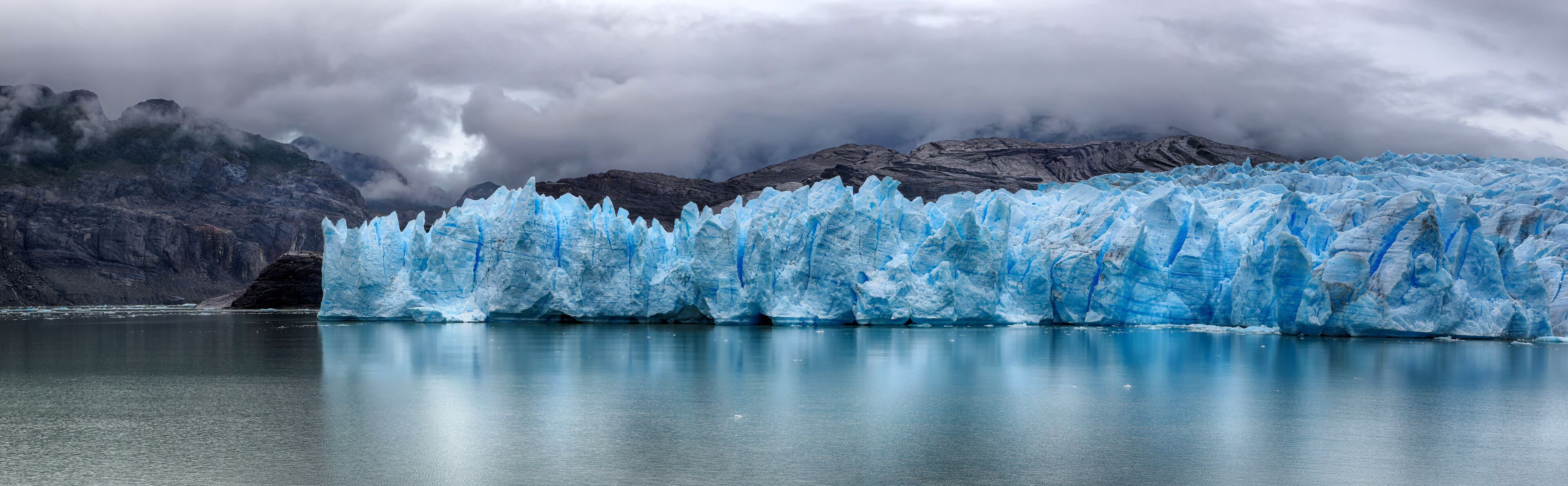 A glacier with sharp edges and a calm body of water in the foreground.