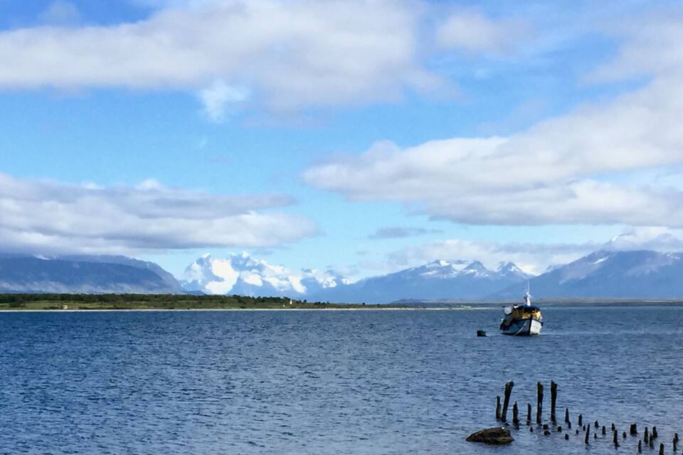 Un lago tranquillo con una piccola barca ancorata vicino alla riva, circondato da montagne e un cielo sereno.