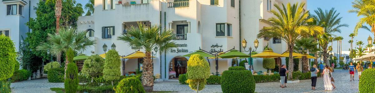 A white building with a café named "Les Jardins" and palm trees in the courtyard.