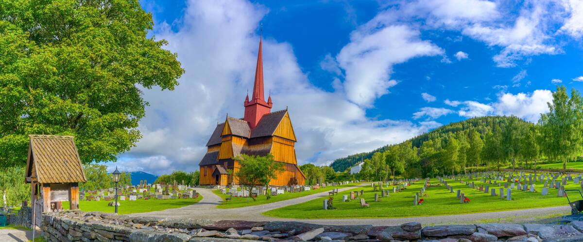 A church with a red spire, a stone wall, and a cemetery with gravestones.