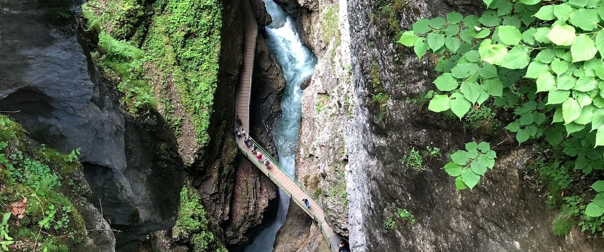 A narrow gorge with a cascading waterfall and a wooden bridge.