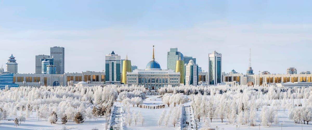 A cityscape with modern skyscrapers, a prominent blue dome, and a snow-covered park.