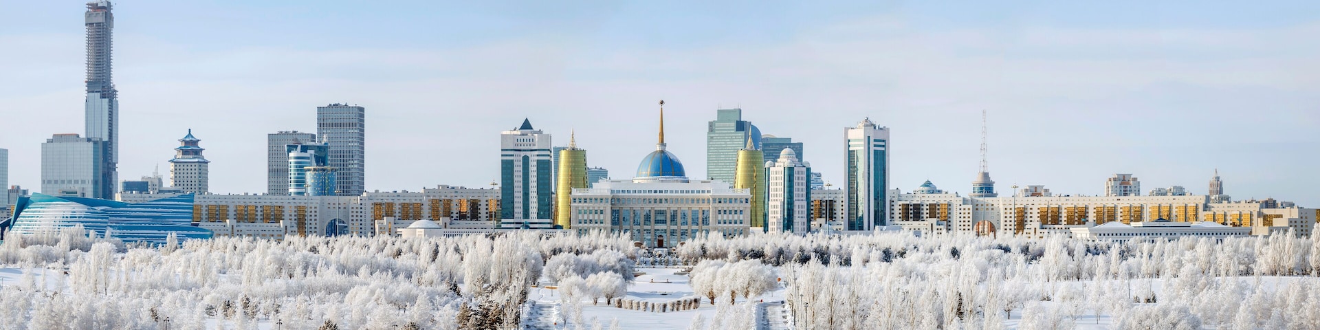 A cityscape with modern skyscrapers, a prominent blue dome, and a snow-covered park.