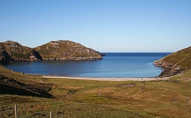 Paisagem costeira com praia, áreas gramadas e colinas rochosas.