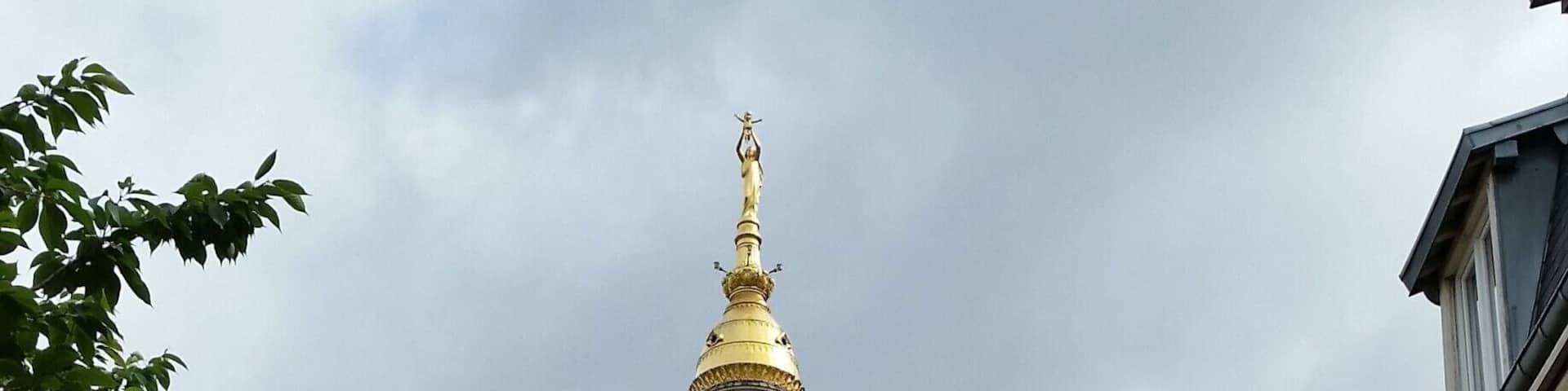 A historic building with a tall tower and a golden spire, surrounded by brick buildings and shops.
