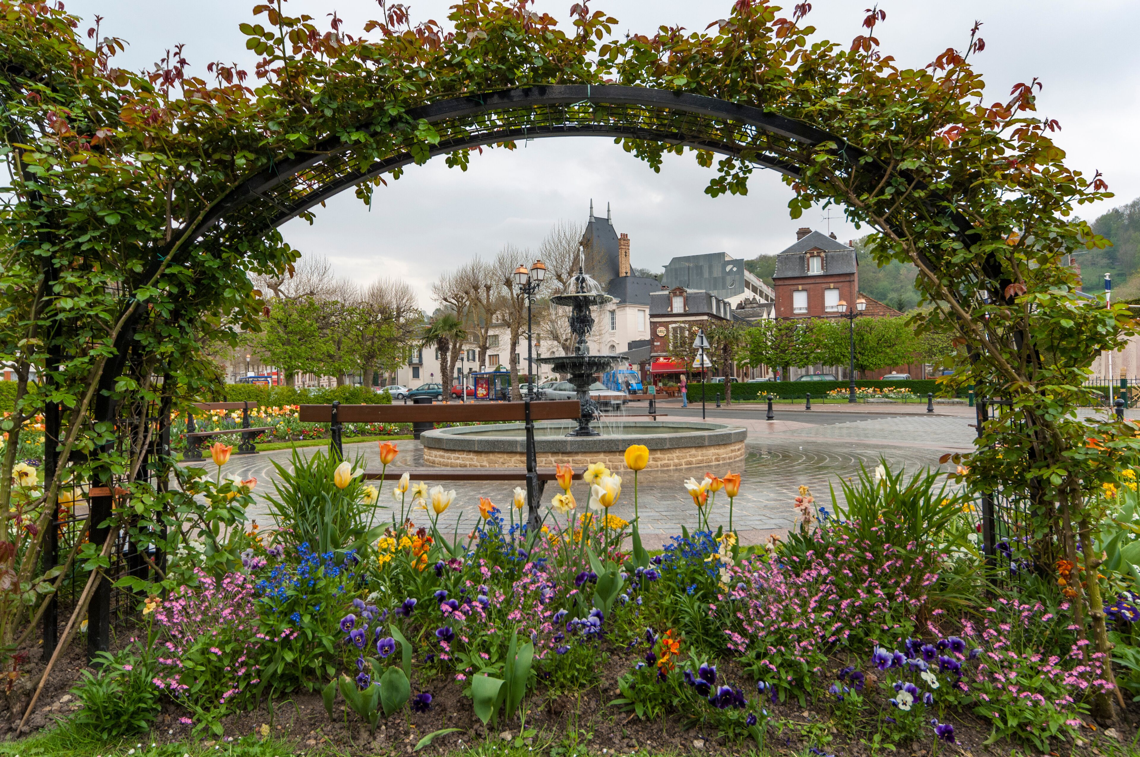 A garden with a fountain, colorful flowers, and a historic building in the background.