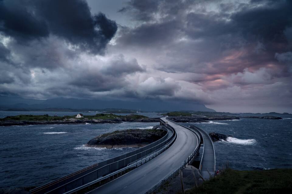 A coastal road curving along the shoreline with a small house on a rocky outcrop.
