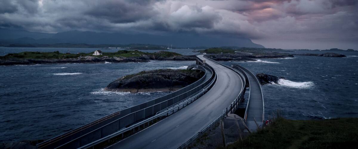 A coastal road curving along the shoreline with a small house on a rocky outcrop.