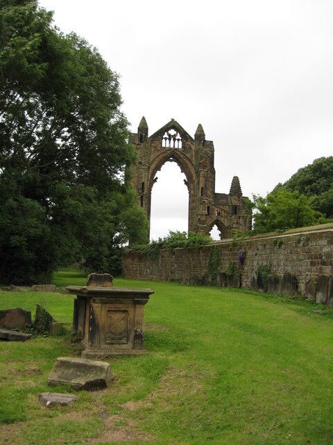 An ancient stone archway surrounded by lush greenery and a stone wall.