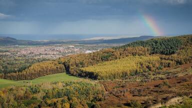 View from the summit of Roseberry Topping, Yorkshires Matterhorn, with a rainbow arcing over Guisborough under a moody sky, North York Moors National Park, UK