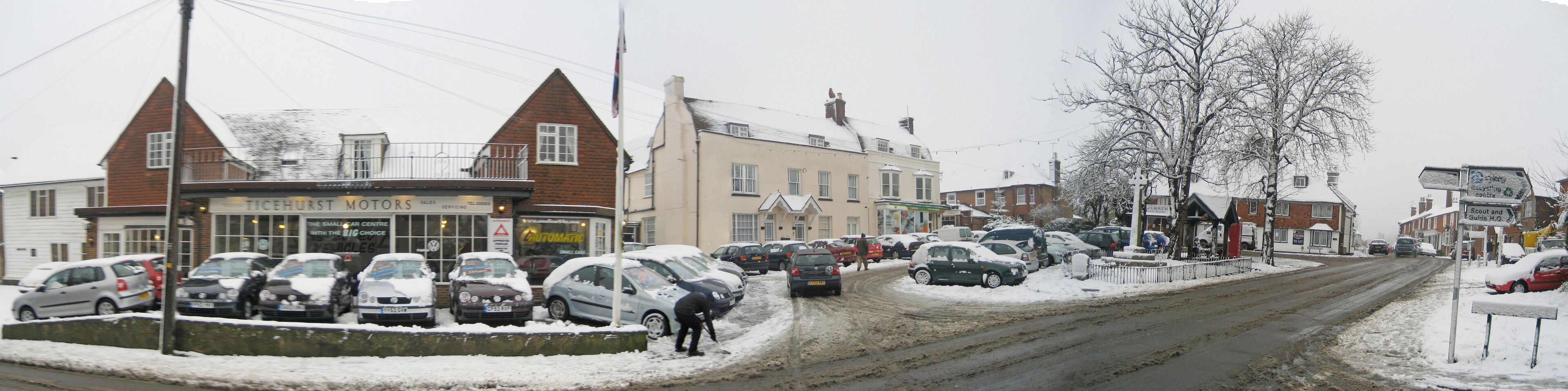 A snowy street with parked cars and buildings, including a motor service center.