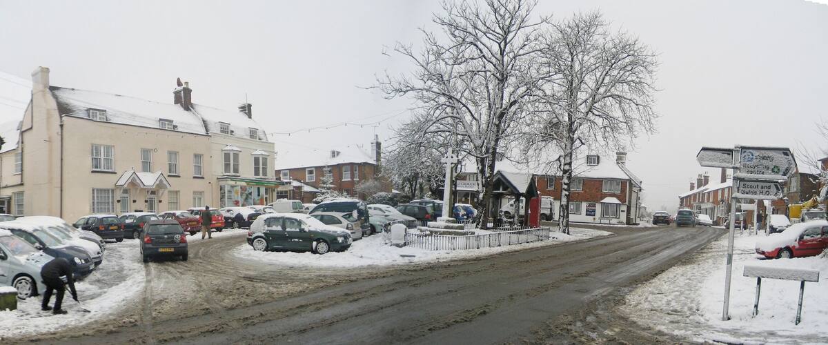 A snowy street with parked cars and buildings, including a motor service center.