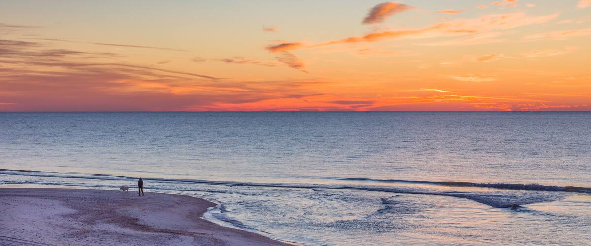 A beach at sunset with a clear sky and calm sea.