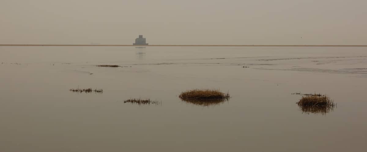 A calm body of water with a small island and a distant ship.