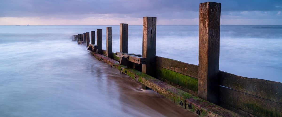 A long pier extending into calm waters with a cloudy sky.