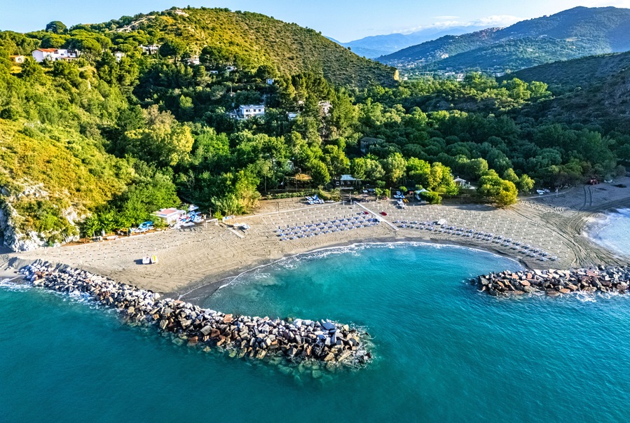 Une zone cĂŽtiĂšre comprenant une plage, une digue rocheuse et une colline avec des bĂątiments.