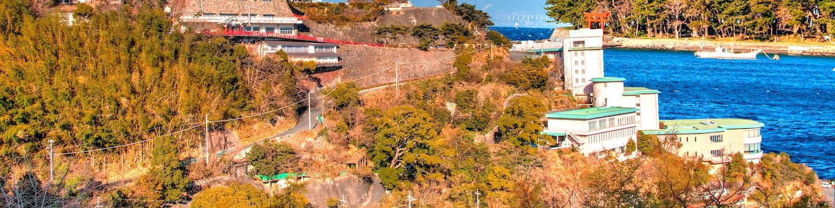 Eine traditionelle japanische Burg, im Hintergrund der Berg Fuji, und eine Küstenlandschaft mit Booten.