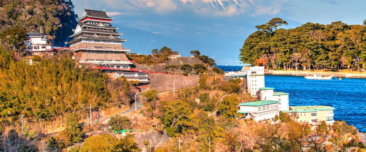 A traditional Japanese castle, Mt. Fuji in the background, and a coastal area with boats.