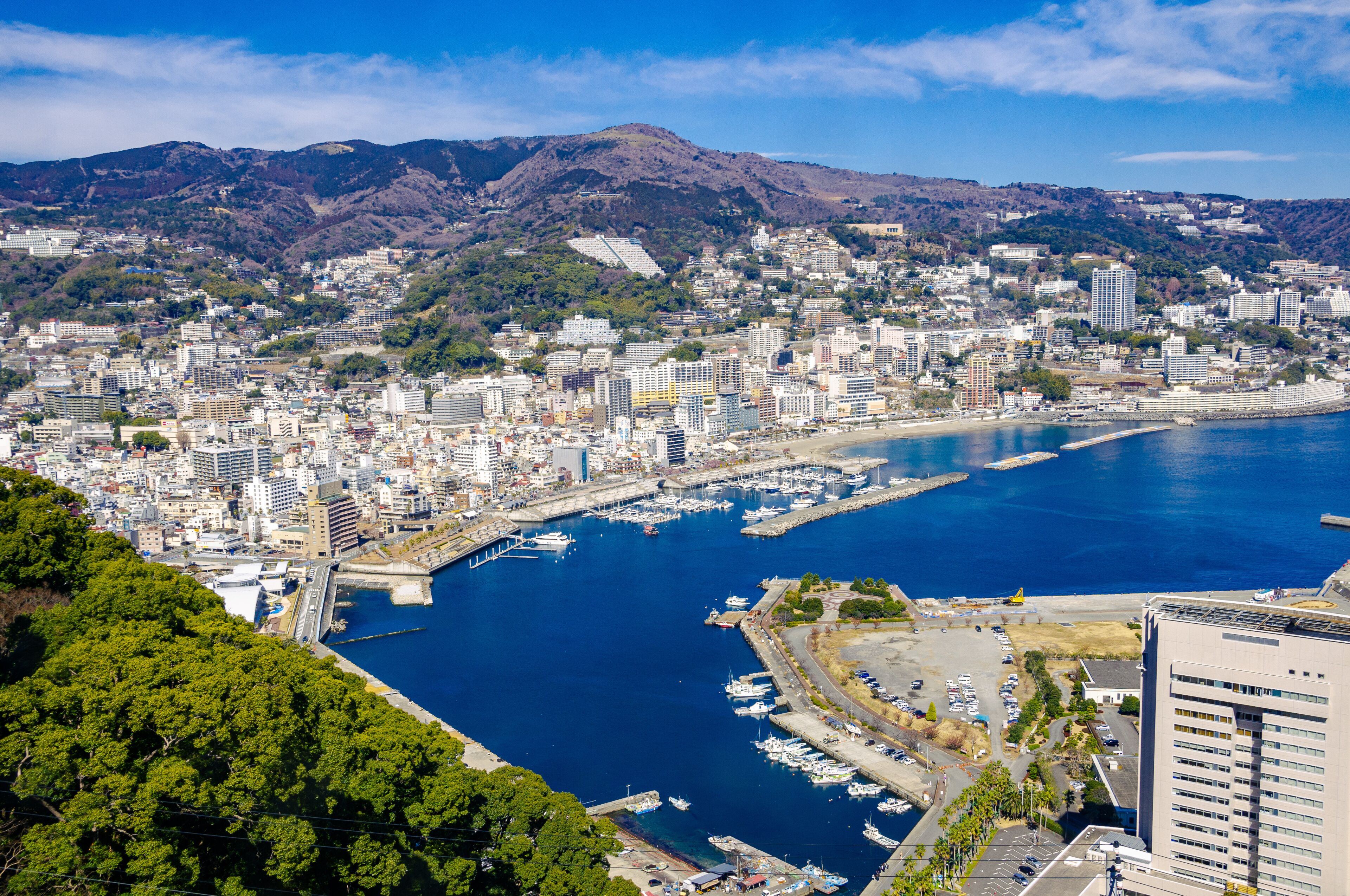 A coastal city with a marina, dense urban buildings, and mountains in the background.