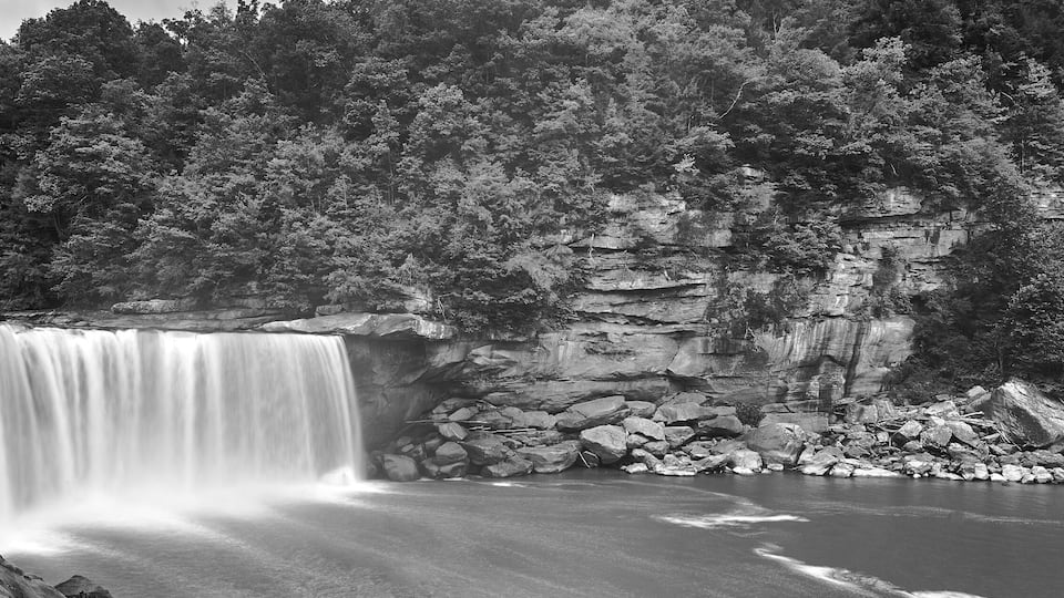 A waterfall cascading into a river surrounded by dense forest and rocky cliffs.
