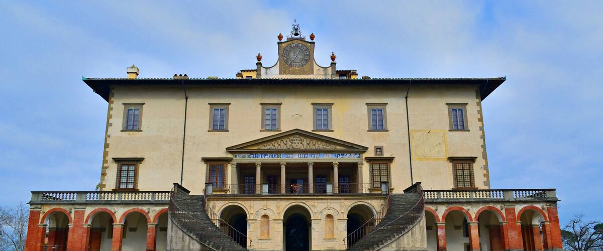 A large, historic building with a central entrance, arched windows, and a clock on the facade.