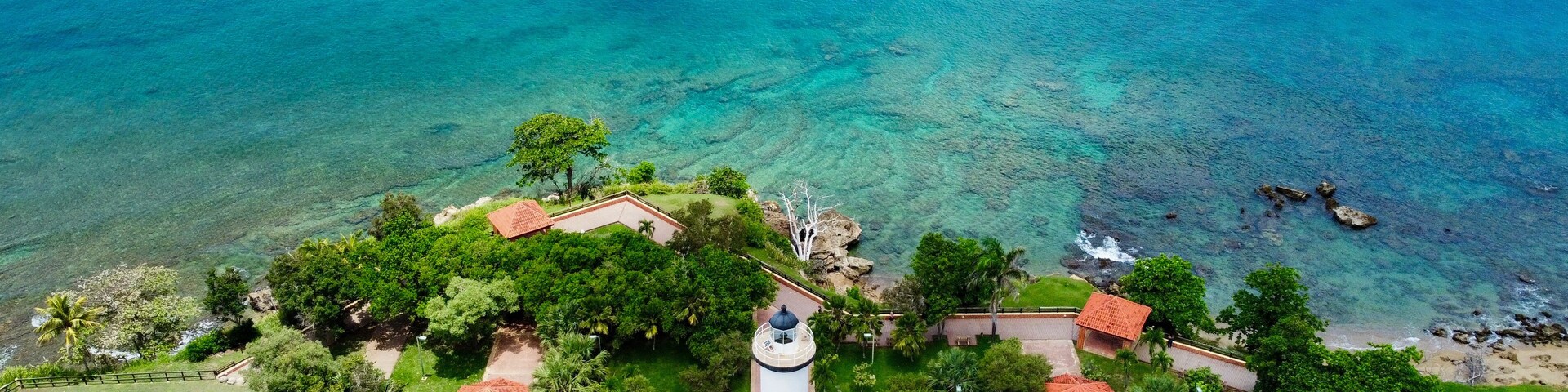 Un paisaje costero con un faro, palmeras y aguas azules cristalinas.