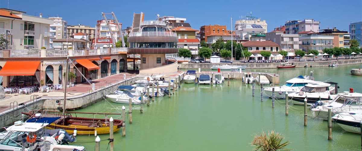 A marina with boats docked, a restaurant with outdoor seating, and buildings with balconies.