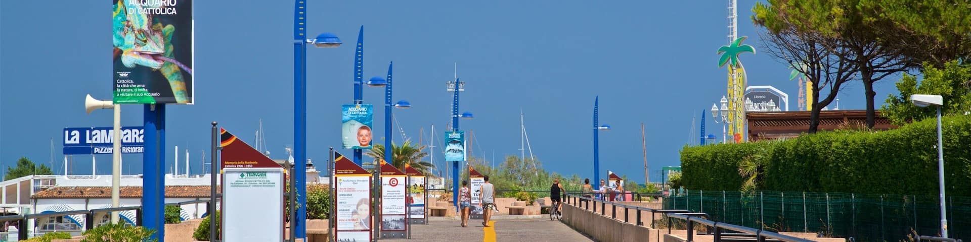 A coastal promenade with blue street lamps, informational signs, and a yellow path.
